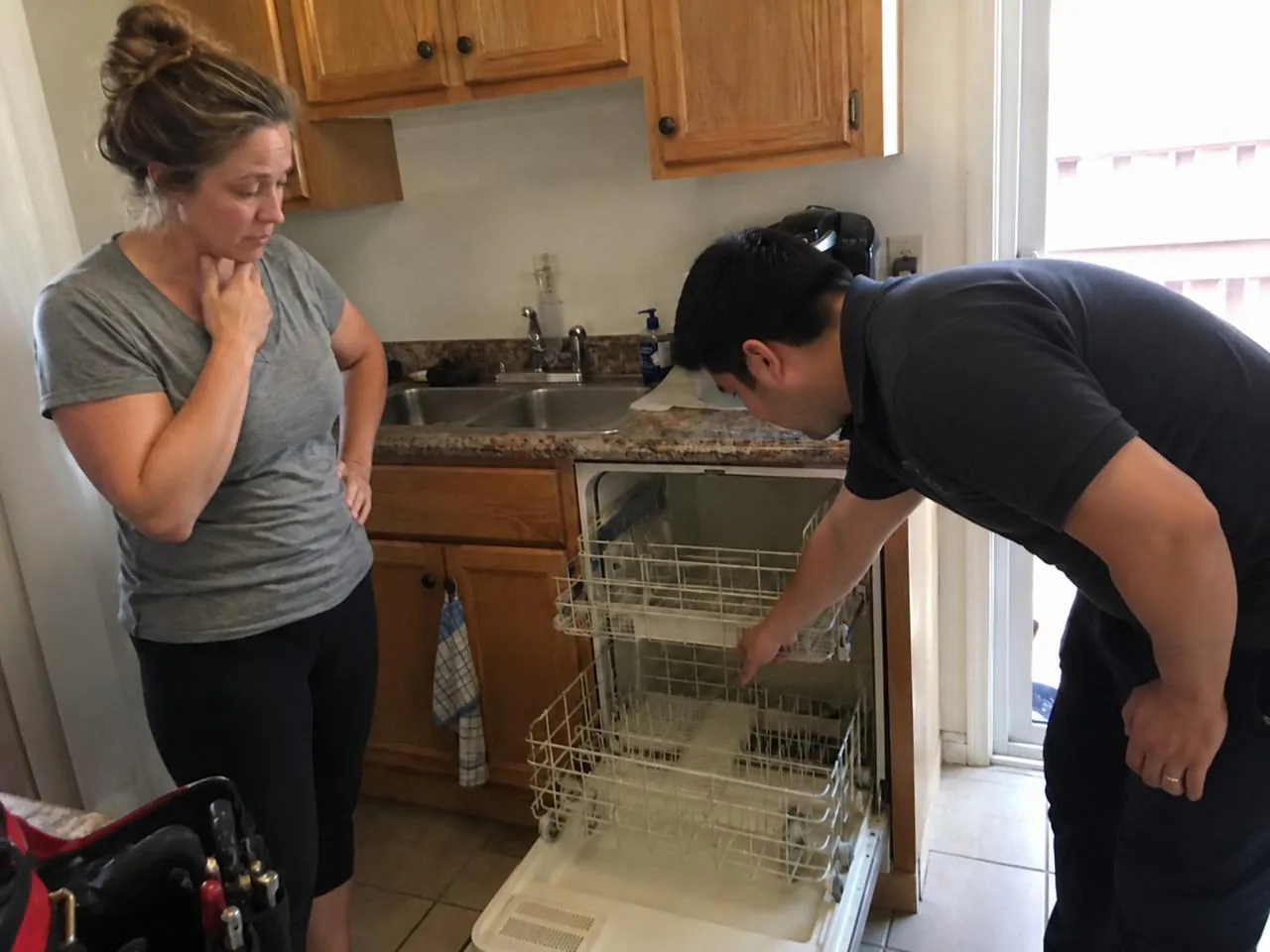 Technician diagnosing an open dishwasher while the homeowner watches